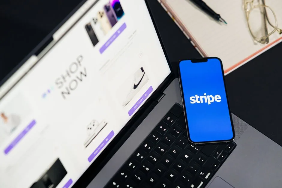 Photo by Julio Lopez on Pexels Mobile phone displaying Stripe app on a laptop with an eCommerce site open, symbolizing online shopping.