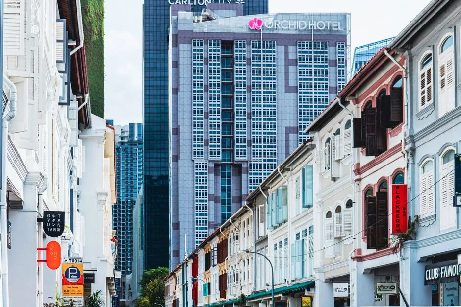 Street view showcasing modern skyscraper behind historical shophouses, blending architectural styles.