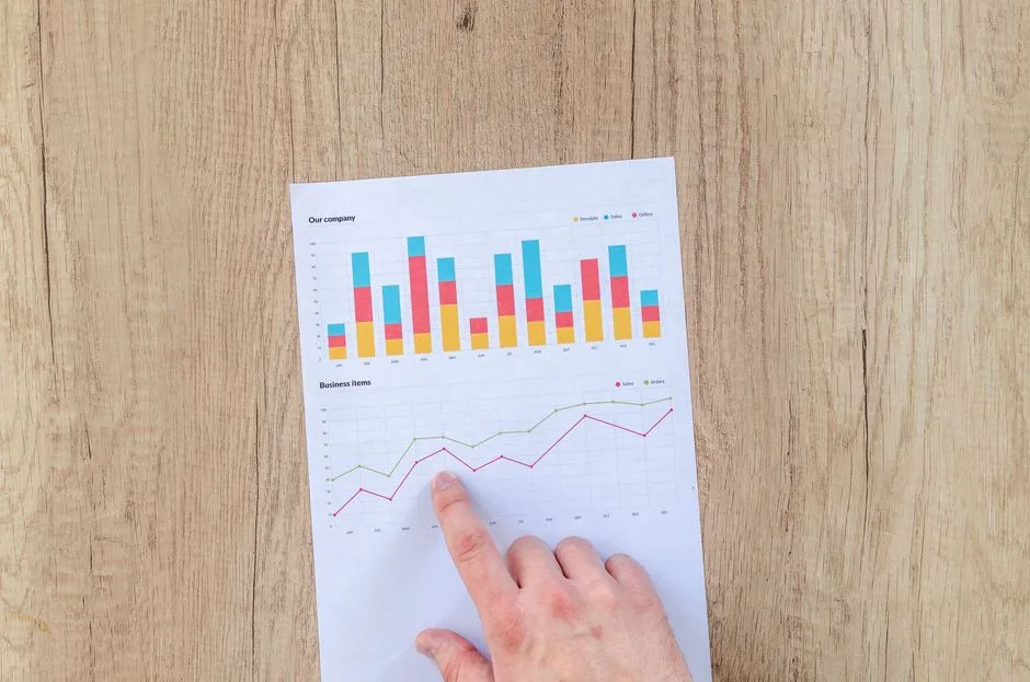 Photo by Lukas Blazek on Pexels A hand points to colorful business charts and graphs on a paper sheet on a wooden desk.
