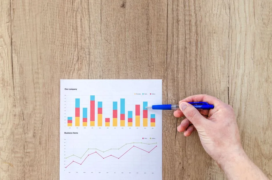 Photo by Lukas Blazek on Pexels A hand points a pen at business graphs on a wooden table, highlighting data analysis.