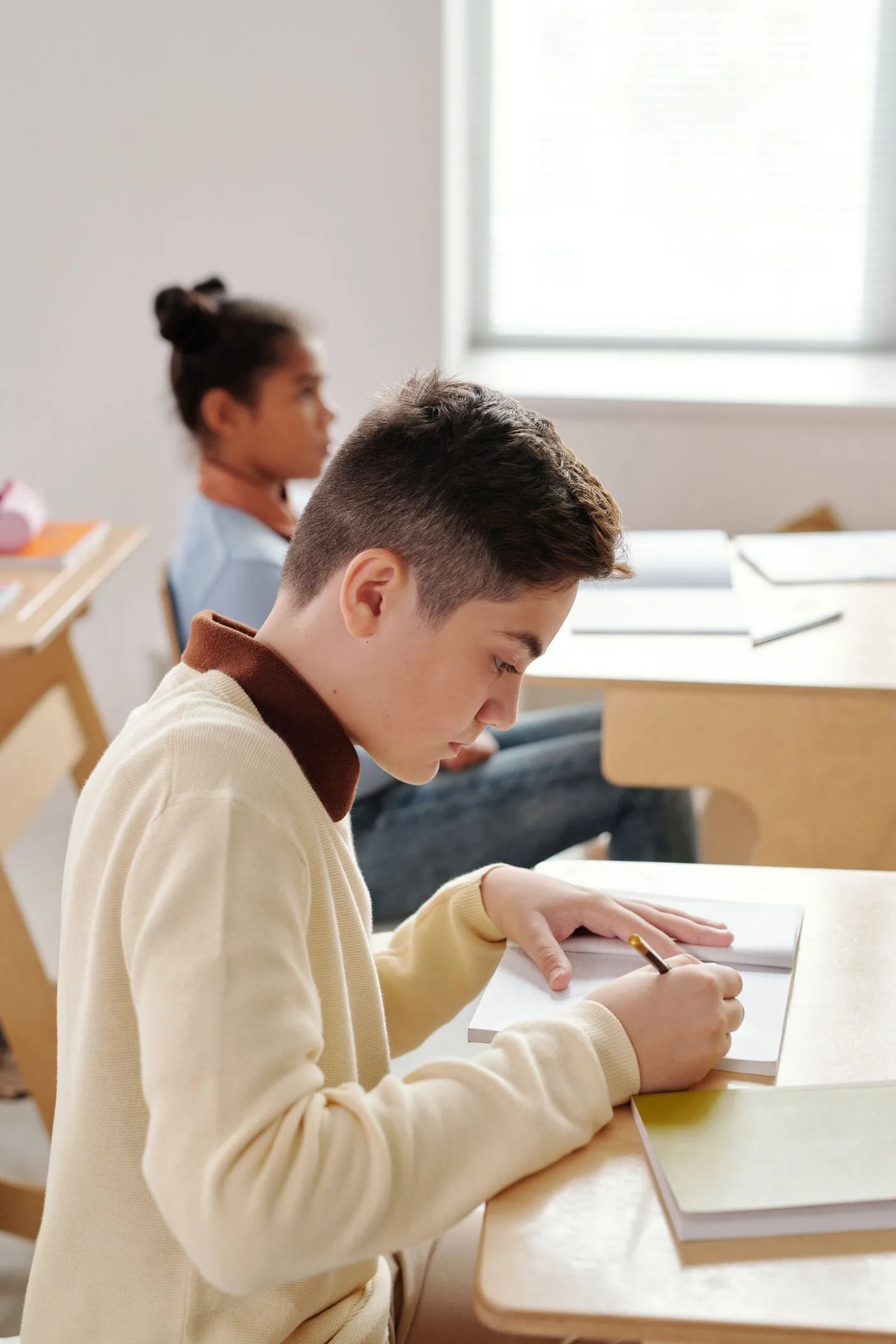 Focused student writing in a notebook in a classroom. Photo by Max Fischer on Pexels