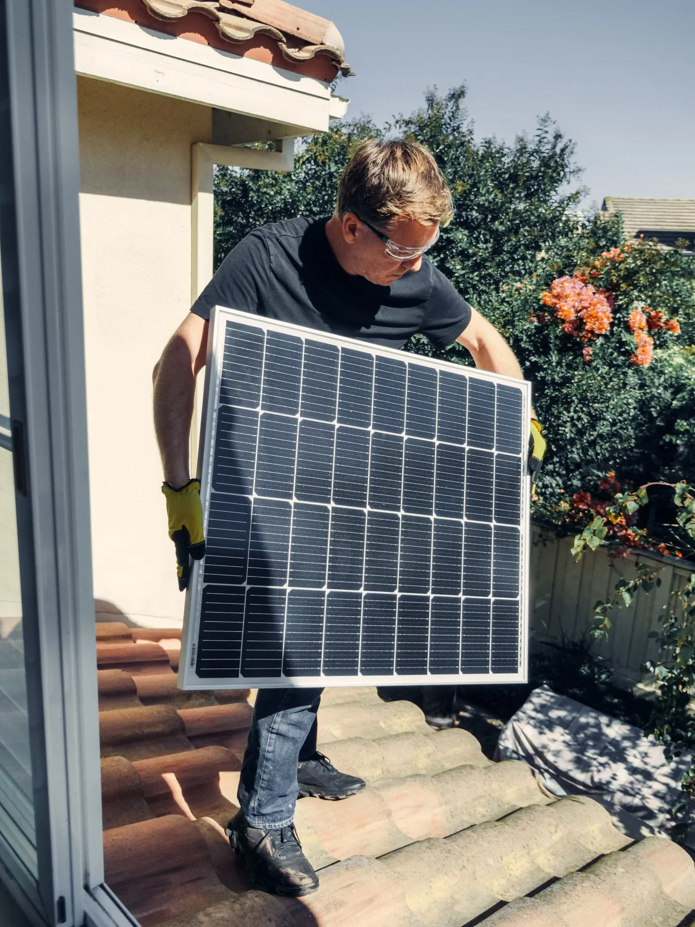 Solar installer carrying a panel onto a residential roof. Photo by Kindel Media on Pexels