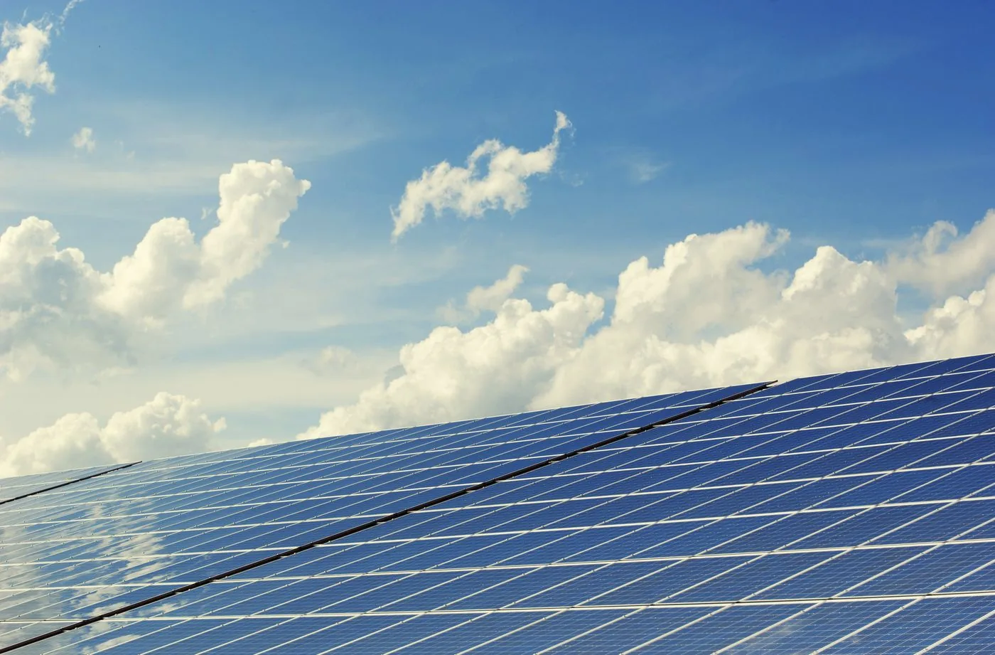 Solar panel array under a bright blue sky with clouds. Photo by Pixabay on Pexels