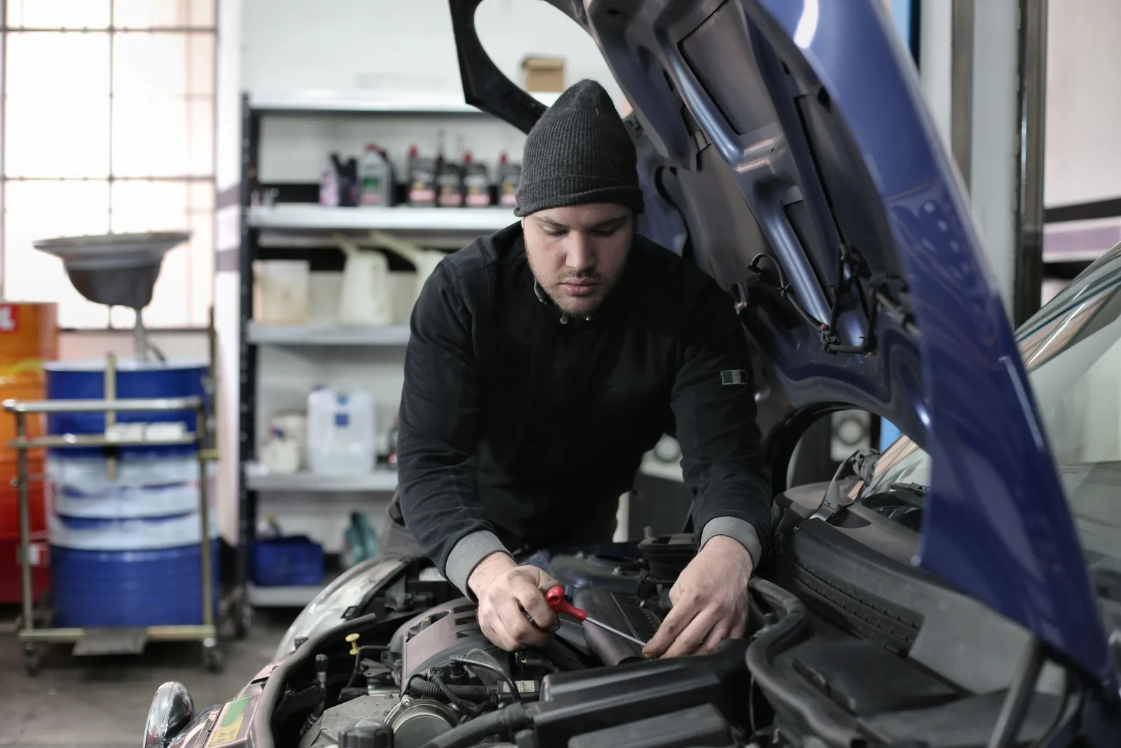 Man working under car hood in a garage, focused on engine repair. Photo by Andrea Piacquadio on Pexels