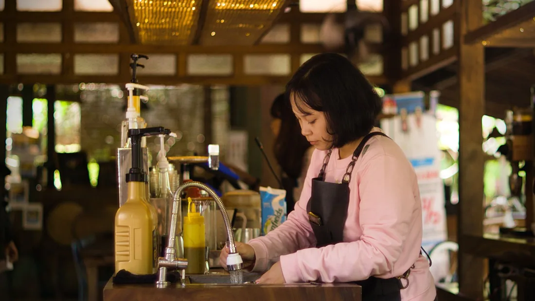A female bartender washing dishes at a cozy, rustic bar with warm lighting in Singapore. Photo by Yudinda Gilang Pramudya on Pexels